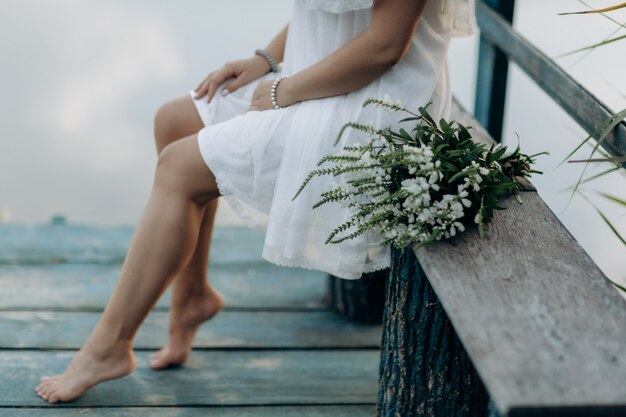 Foto donna su un ponte di legno sul lago con un mazzo di fiori di campo