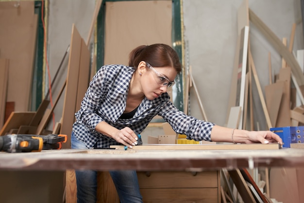 Falegname donna con tavola di legno dietro il banco di lavoro in officina