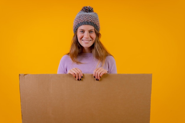 Photo a woman in a wool cap holding a cardboard sign on a yellow background