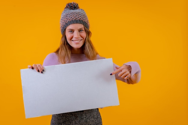 Woman in a wool cap holding a white sign on a yellow background