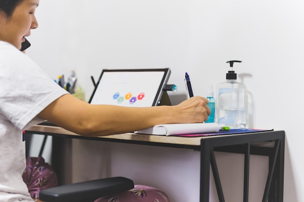 Woman work from home talking on cell phone while taking note.