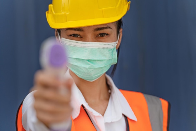 Photo woman worker in mask face and using measures temperature with a noncontact infrared thermometer