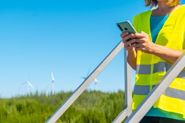 Lavoratrice in una revisione tecnica dell'energia verde del parco eolico con il telefono in mano