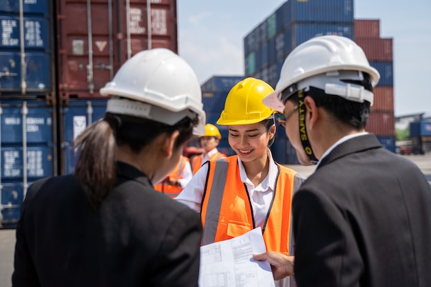 Foreman과 함께 일하는 여성 노동자, 노란색 헬멧을 착용하여 선적을 제어하고 조선소 또는 항구에서 수입 및 수출을 위해화물 화물선에서 컨테이너의 품질을 확인합니다.