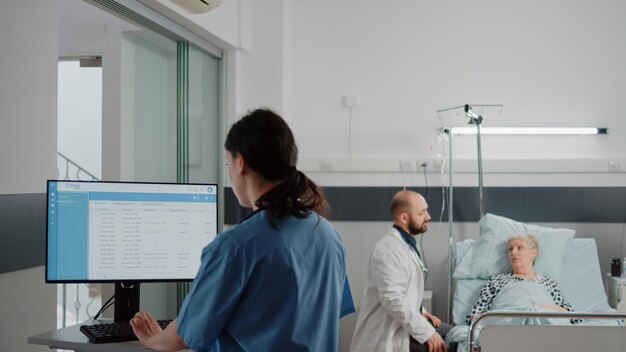 Woman working as nurse and looking at computer with files for healthcare checkup. medical assistant using patient documents on monitor for support and recovering assistance on desk