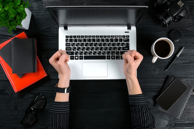 Фото Женщина, работающая за офисным столом. вид сверху человеческих рук, клавиатуры ноутбука, чашки кофе, смартфона, ноутбука и цветка на фоне деревянного стола.