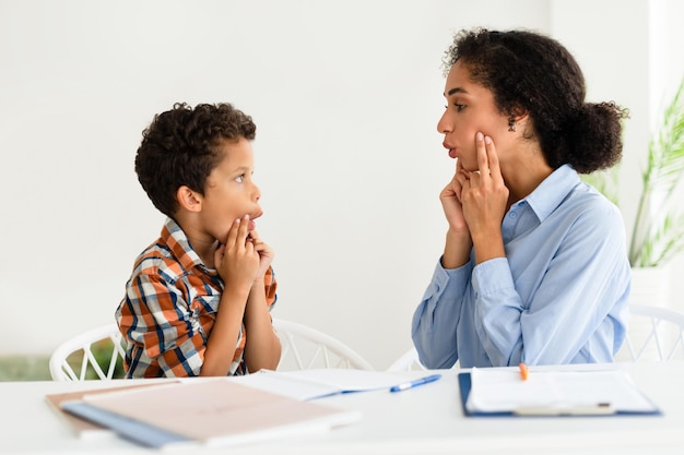 Photo woman working on boy pronunciation at speech therapy session indoors