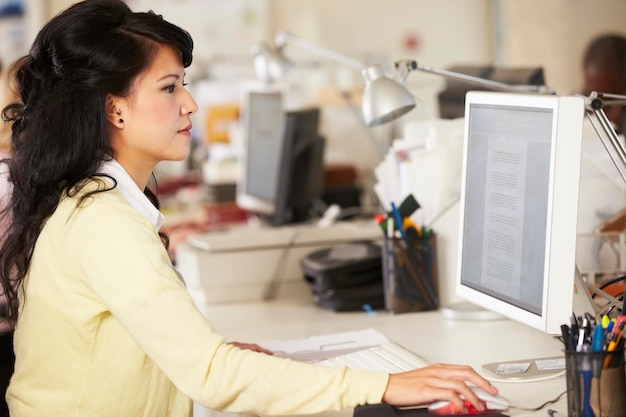 Woman Working At Desk In Busy Creative Office