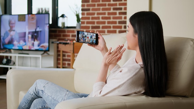 Woman working from home while discussing with coworkers on\
internet conference using smartphone. person working remotely while\
in online meeting videocall on phone sitting in apartment.