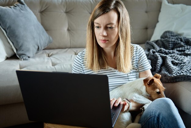 Woman working from home with pet dog using laptop