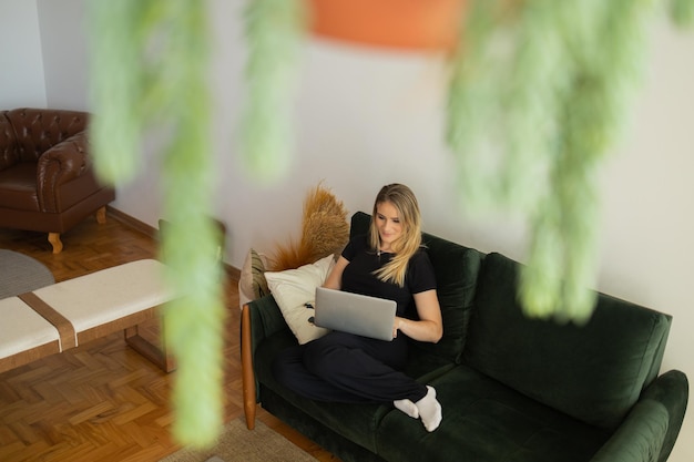 Woman working at home from couch with laptop on her lap home office concept gray notebook