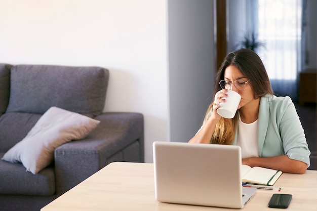 Woman working at home with laptop and drinking coffee.