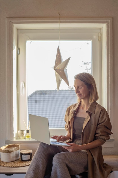 Woman working at home with laptop sitting on table near window