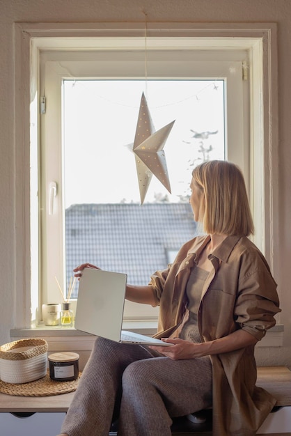 Woman working at home with laptop sitting on table near window