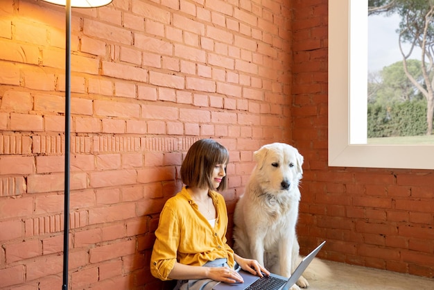 Woman working on laptop computer while sitting with her dog at home