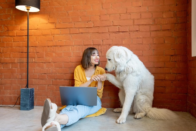 Женщина работает на ноутбуке, сидя дома со своей собакой