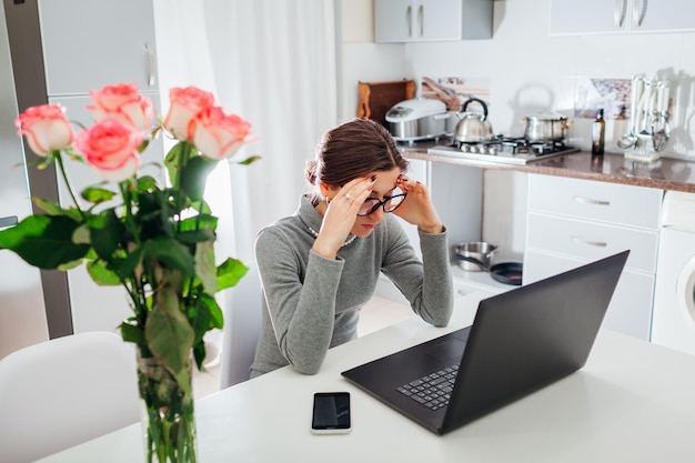 Woman working on laptop on modern kitchen young tired freelancer having headache