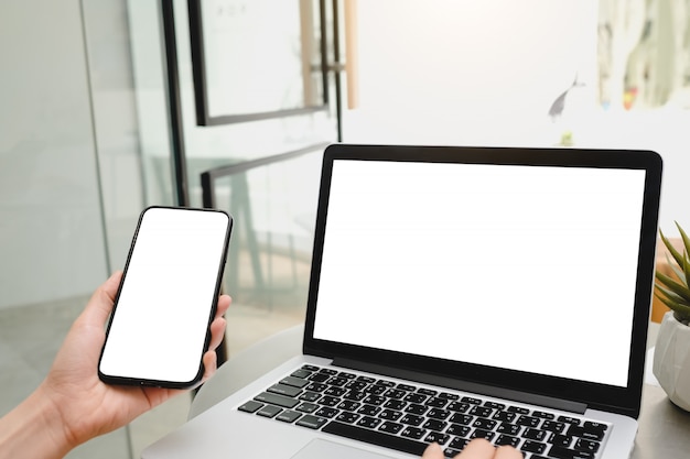 Woman working on laptop and  phone with white screen in cafe.