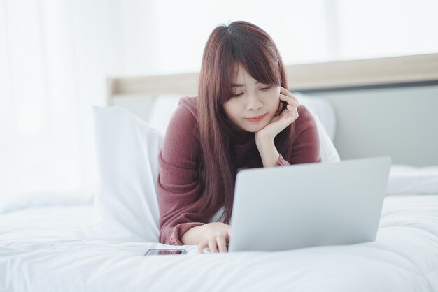 Woman working on a laptop sitting on the bed in the house.