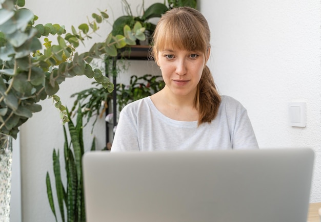 Woman working on laptop surrounded by plants and flowers on balcony at daytime