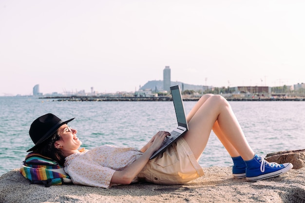 海のそばでコンピューターと横になって働く女性