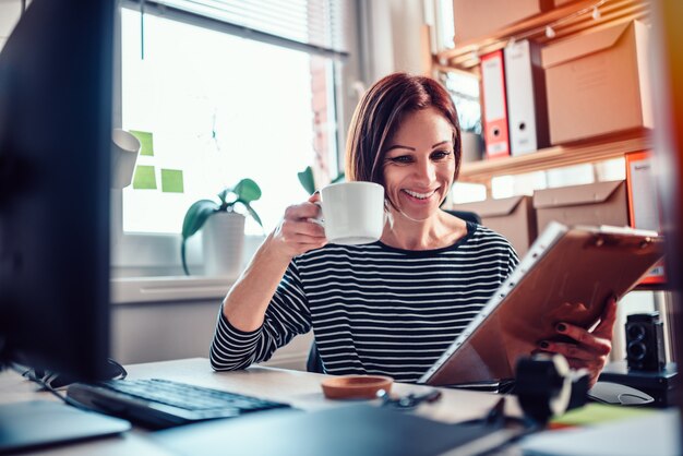 オフィスで働いて、コーヒーを飲む女性