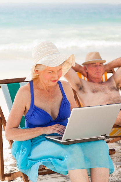 그녀의 남편이 해변에서 자고있는 동안 그녀의 노트북에서 일하는 여자