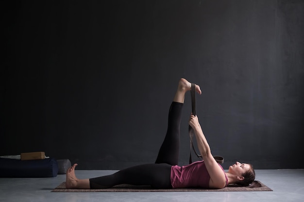 Woman working out using yogic belt lying in yoga Supta Padangushthasana