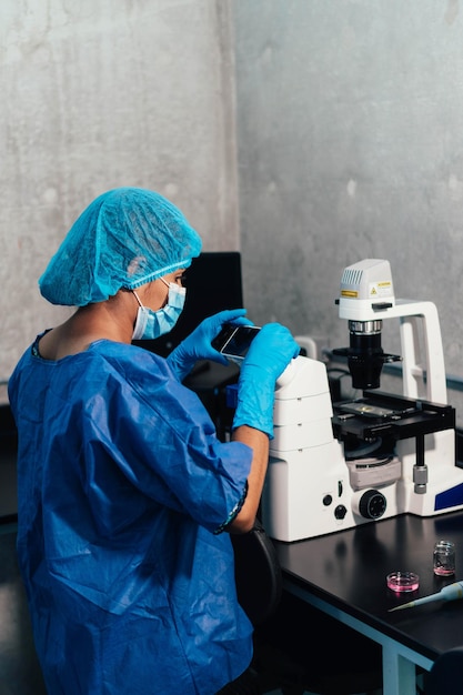 Женщина, работающая в профессиональной лаборатории с сотовым телефоном и микроскопом