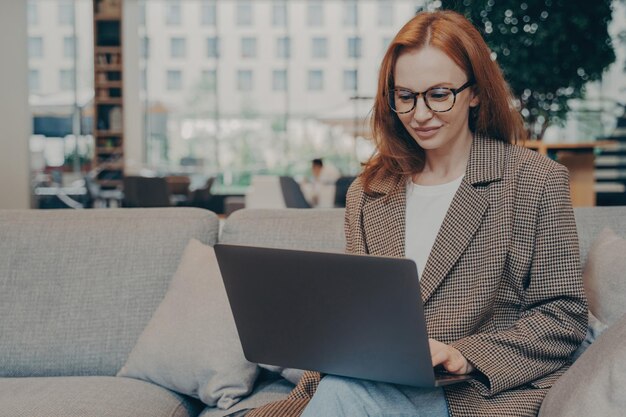 Photo woman working remotely in coworking space using laptop while sitting on couch