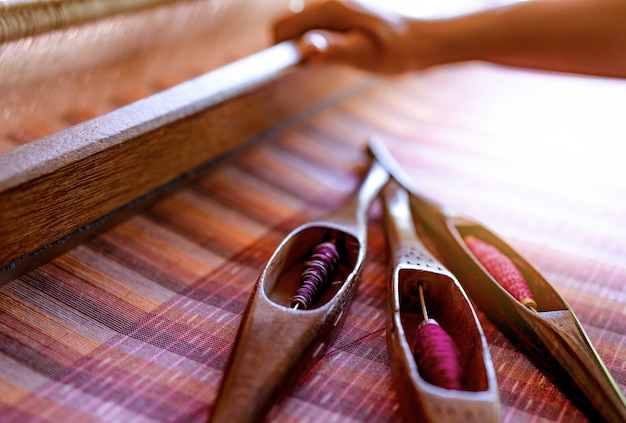 Woman working on weaving machine for weave handmade fabric. Textile weaving. Weaving using traditional hand weaving loom on cotton strands.