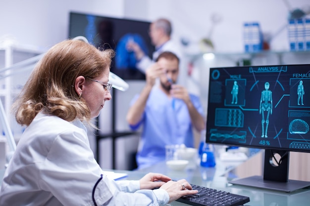 Woman working with computer in the office of a science laboratory. Male scientist working with test tubes in the background.