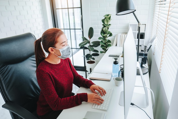 Woman working with computer wearing protective mask