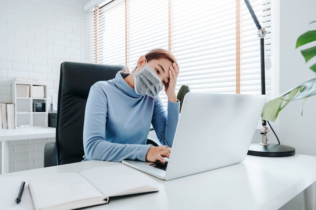 Woman working with computer wearing protective mask