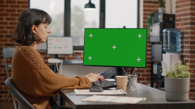 Woman working with horizontal green screen on monitor in startup business office. Entrepreneur using chroma key with isolated mockup template and background on computer display.