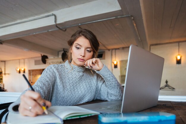 Woman working with laptop computer and notepad in cafe