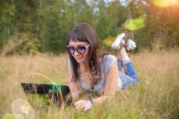 Woman working with a laptop in the middle of a a field in summer.