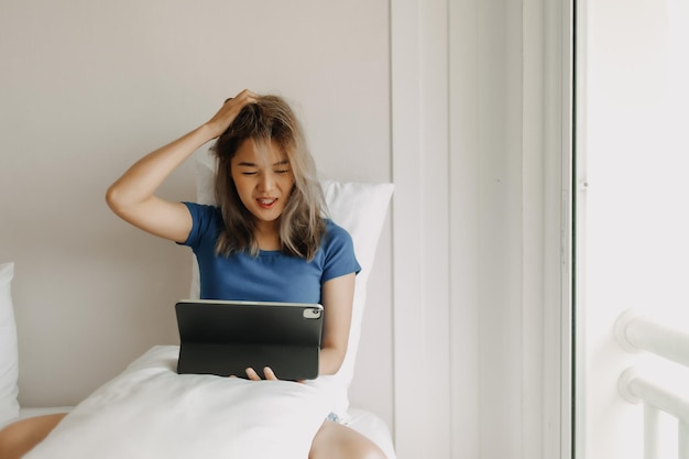 Woman works digital online on her bed feeling tired on vacation