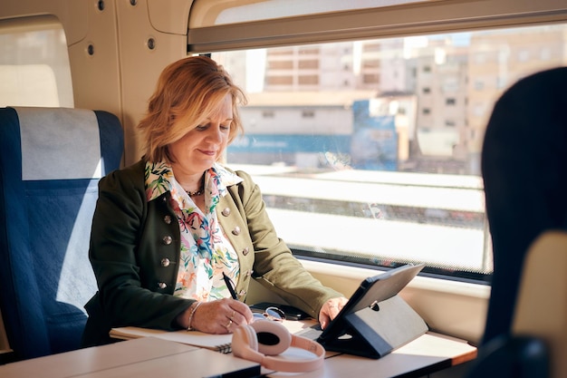 Woman works from a train with a tablet and a notebook Working remotely travel