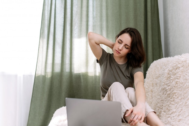 Una donna lavora a casa con un laptop e si strofina il collo per il dolore