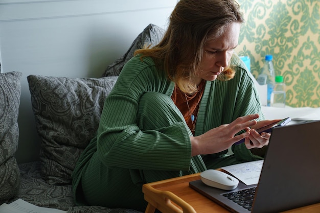 The woman works on a laptop at home in bed work on sick leave