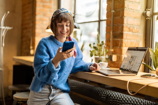 Woman works on phone and laptop at coffee shop