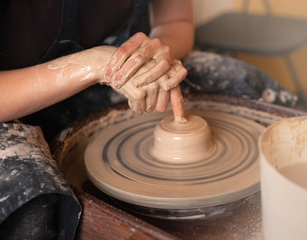 女性がろくろで作業する手がろくろで湿った粘土のカップを形成する芸術的概念