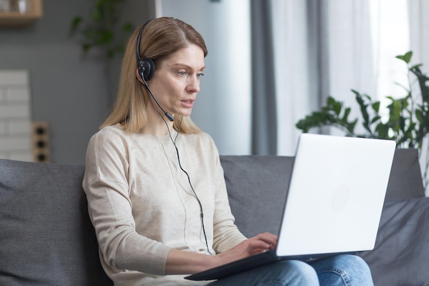 The woman works remotely at home as an online consultant uses a headset and laptop for a video call
