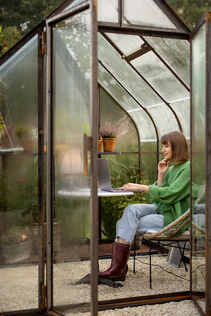 Woman works remotely on laptop in glasshouse at backyard