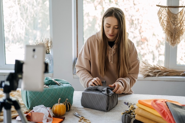 Woman wraps furoshiki gift in zero waste style and record vlog master class on cell phone furoshiki