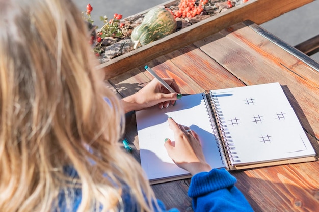 Photo woman writes in a notebook with her left hand, view from behind