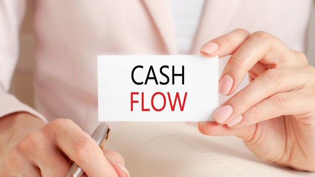 Woman writes in a notebook with a silver pen and hand hold card with text: cash flow.