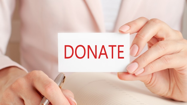 Photo woman writes in a notebook with a silver pen and hand hold card with text: donate