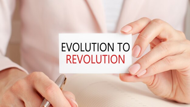 Woman writes in a notebook with a silver pen and hand hold card with text: evolution to revolution.